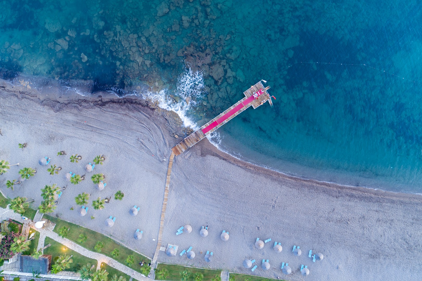 Skats no putna lidojuma uz Flora Garden Beach koka laipu un pludmali — dzidrs tirkīza ūdens un sakopta atpūtas zona