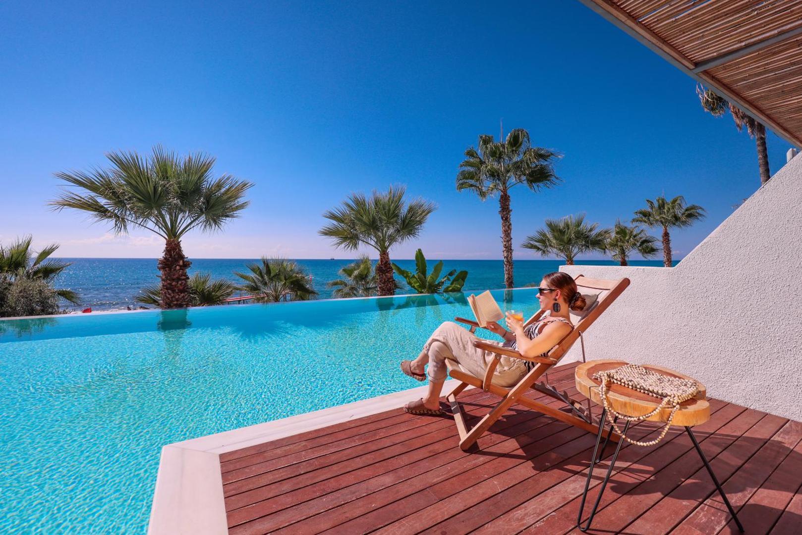 Flora Garden Beach viesnīcas terase ar privāto baseinu, kur sieviete atpūšas krēslā ar grāmatu, fonā palmas un Vidusjūra Turcijā.