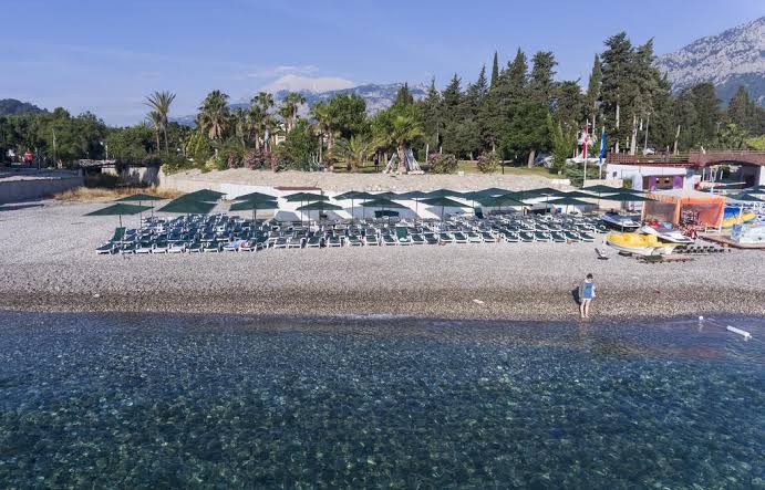 Skats no putna lidojuma uz Kemer Dream Hotel pludmales zonu ar daudziem saulessargiem un caurspīdīgu Vidusjūras ūdeni Kemeras reģionā