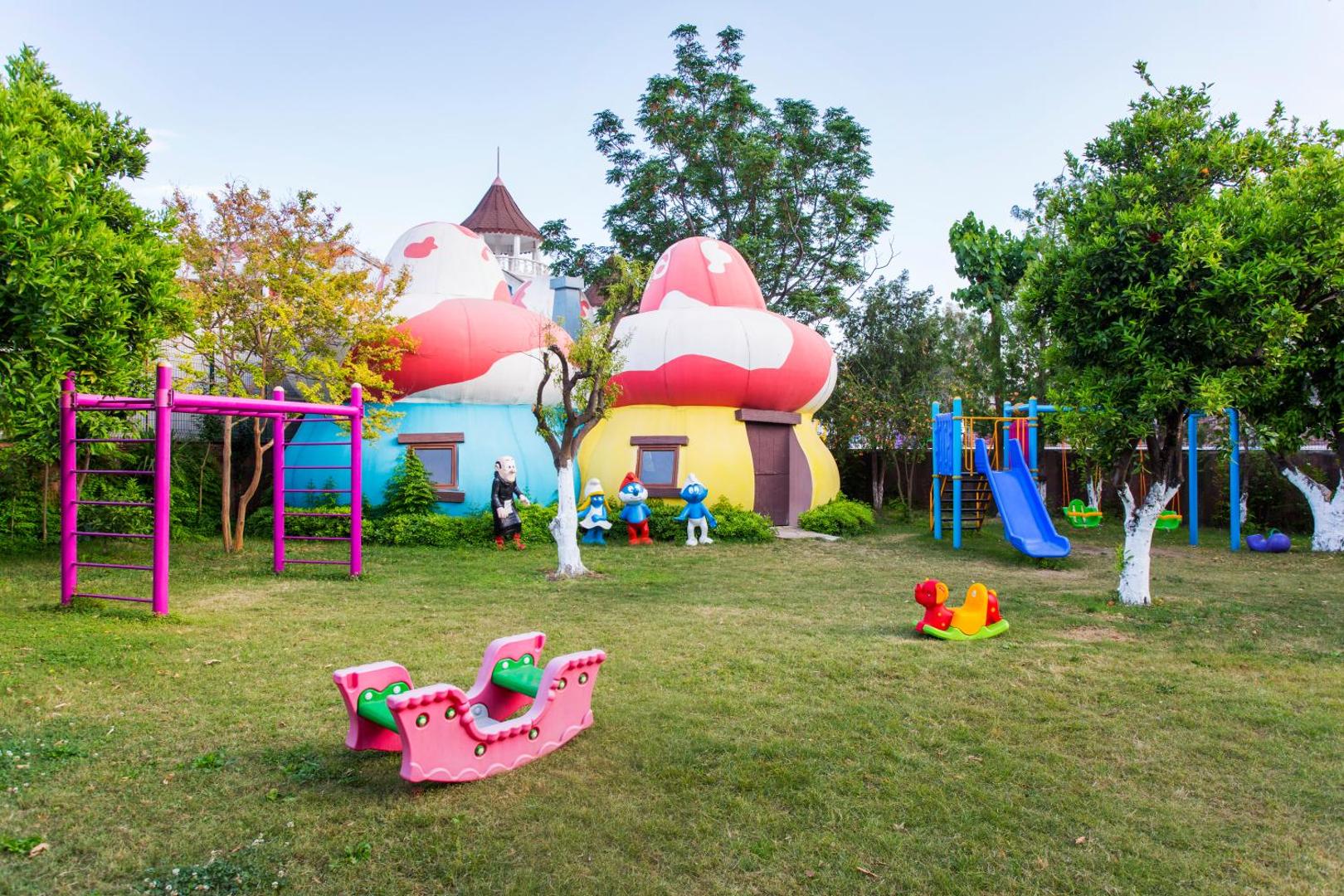 Kemer Dream Hotel bērnu rotaļu laukums ar krāsainām sēņu mājiņām, slidkalniņu un šūpolēm zaļā dārzā Kemeras reģionā.