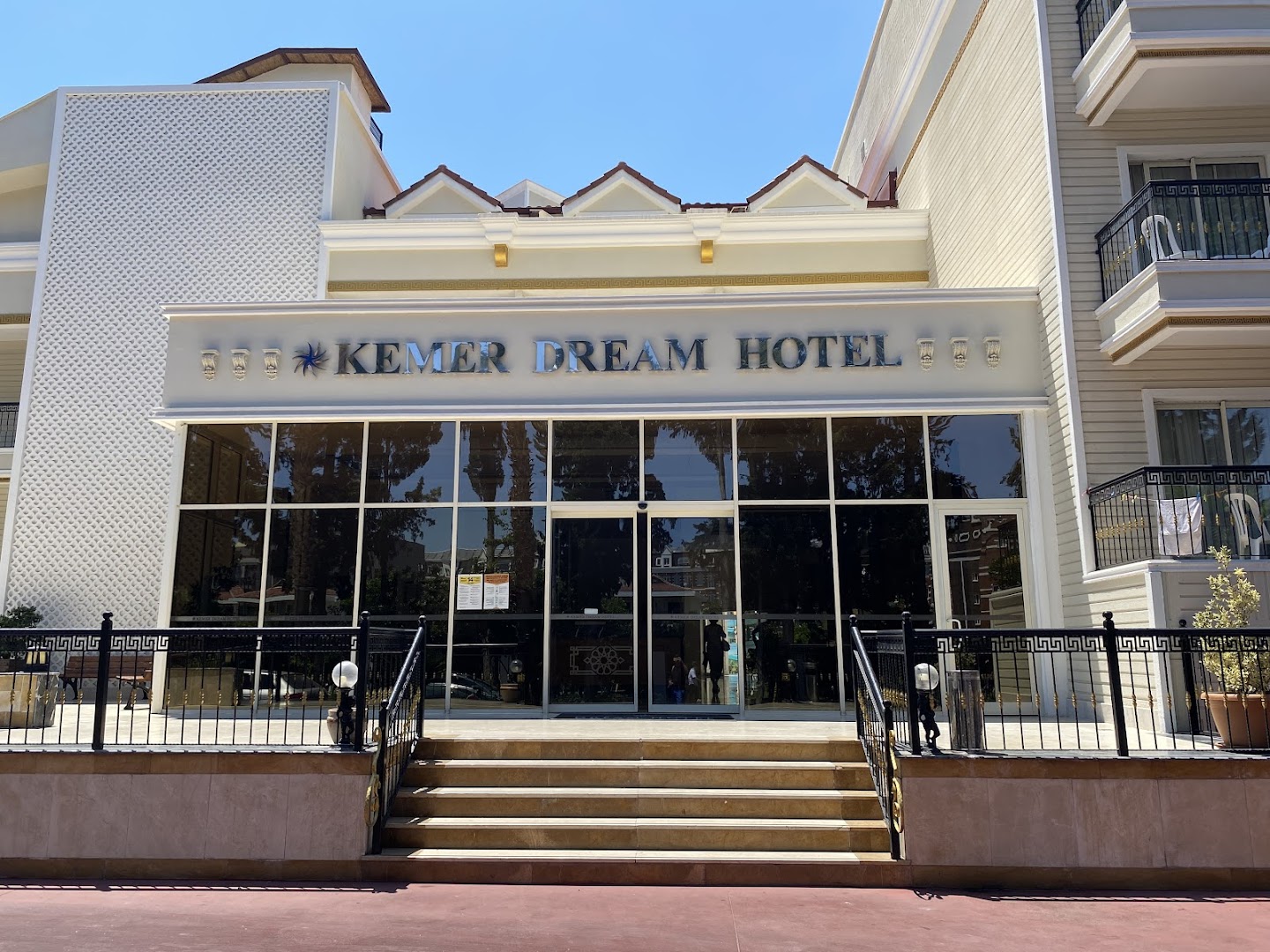 Kemer Dream Hotel galvenā ieeja ar stiklotu fasādi un viesnīcas nosaukumu virs kāpnēm gaišā dienas laikā.