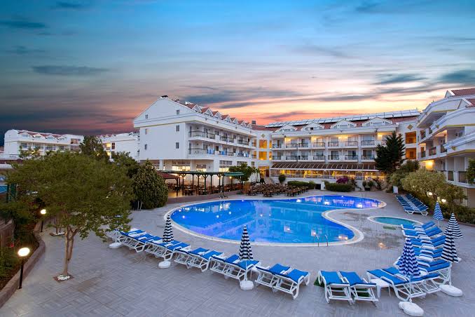 Kemer Dream Hotel teritorijas skats no augšas saulrietā ar baseinu, sauļošanās zonu un apkārtējiem kokiem Kemerā