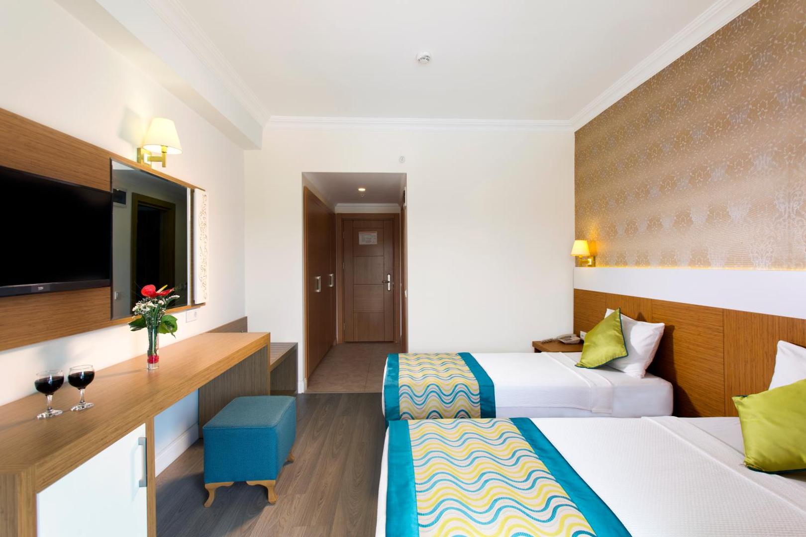 Kemer Dream Hotel numura interjers ar divām gultām, darba virsmu, spoguli un televizoru Kemeras kūrortā