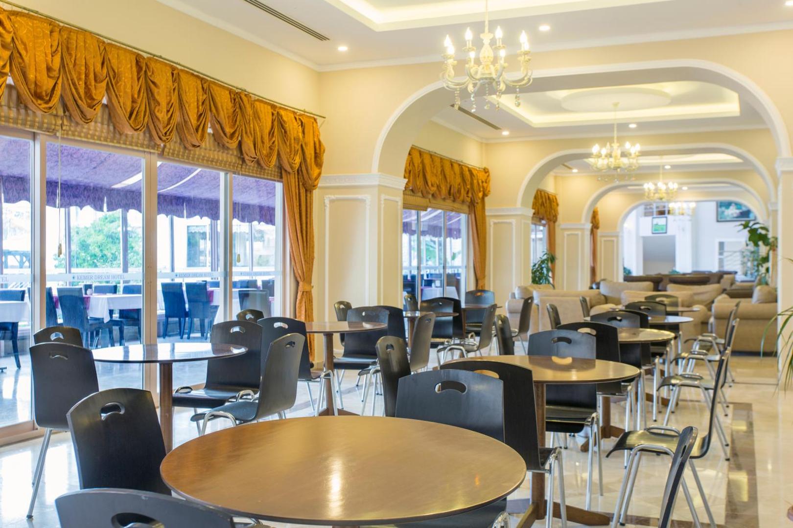 Kemer Dream Hotel lobby bāra zona ar apaļiem galdiem, melniem krēsliem un greznām lustrām iekštelpās pie terases.