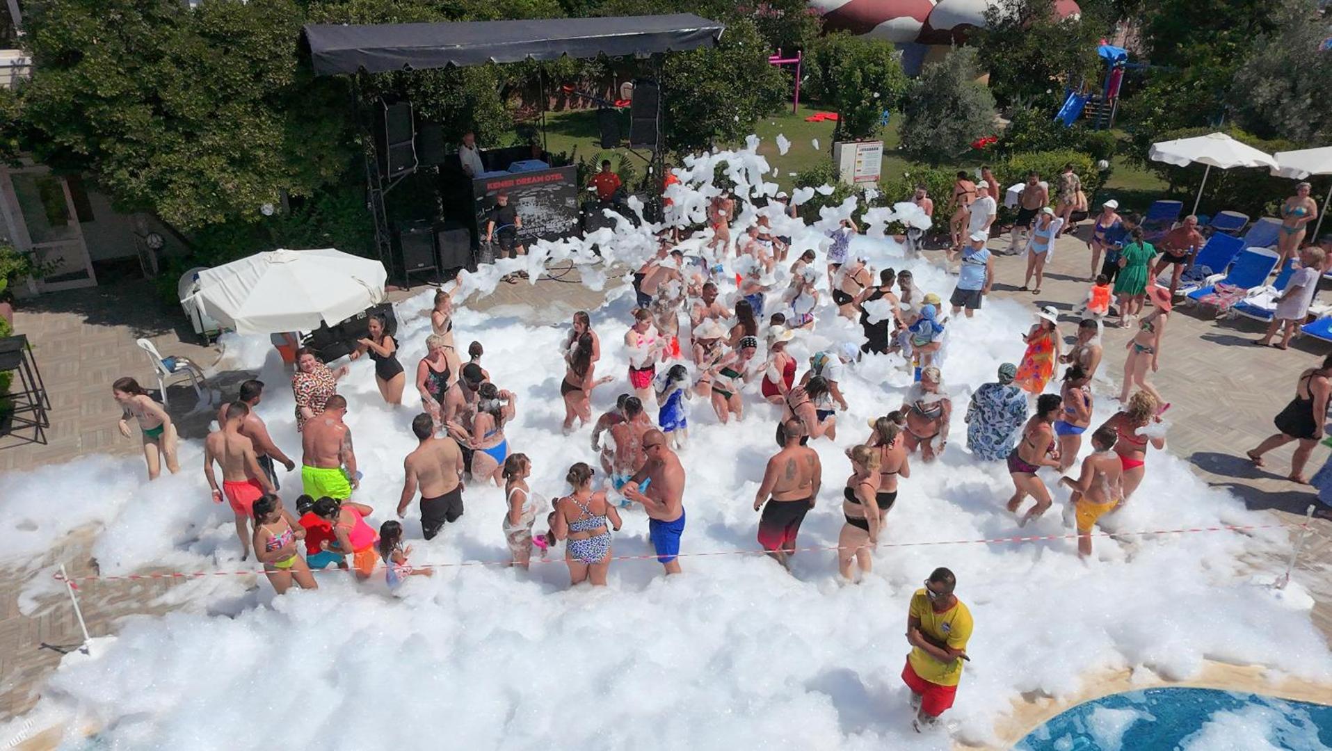 Kemer Dream Hotel putu ballīte pie āra baseina ar daudziem viesiem un dīdžeju saulainā dienā Kemeras kūrortā.
