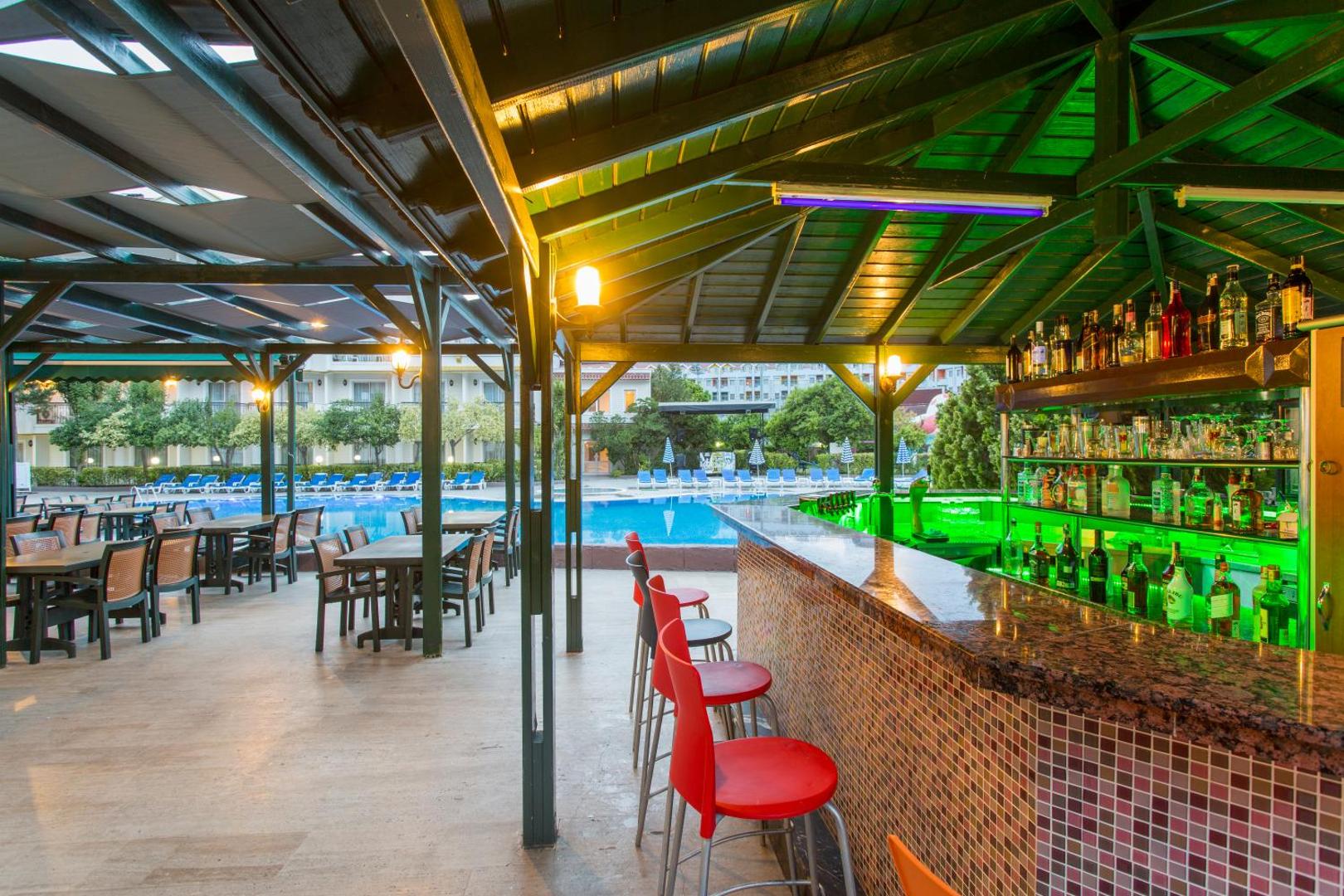 Kemer Dream Hotel āra bārs pie baseina ar sarkanajiem bāra krēsliem un skatu uz peldbaseinu vakara apgaismojumā.