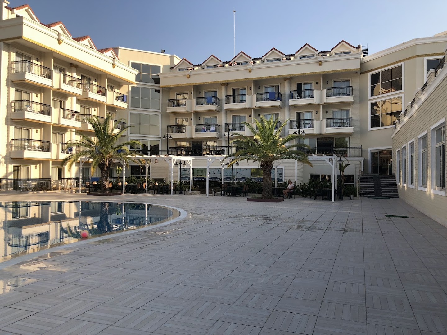 Kemer Dream Hotel iekšpagalms ar baseinu, palmām un atpūtas zonu pie viesnīcas numuru korpusa pēcpusdienas saulē.