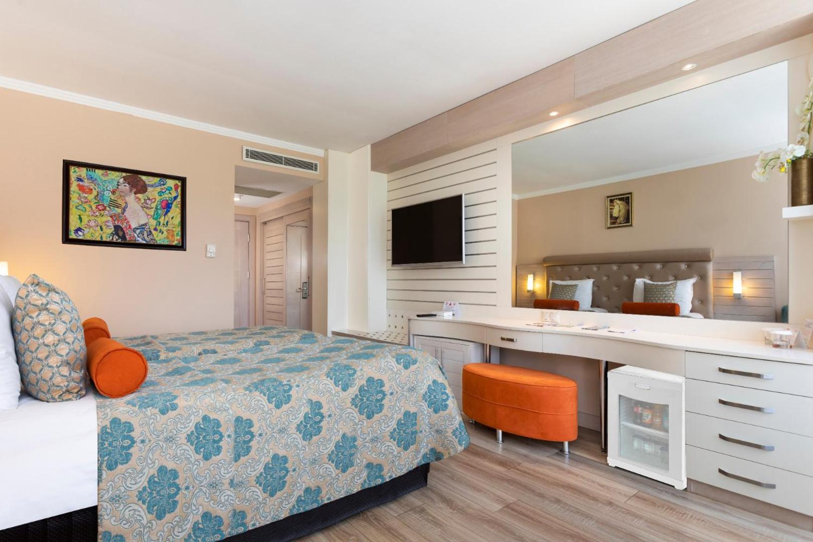 Orange County Kemer numura interjers ar plašu spoguli, darba virsmu, mini ledusskapi un dekoratīvu gleznu pie sienas