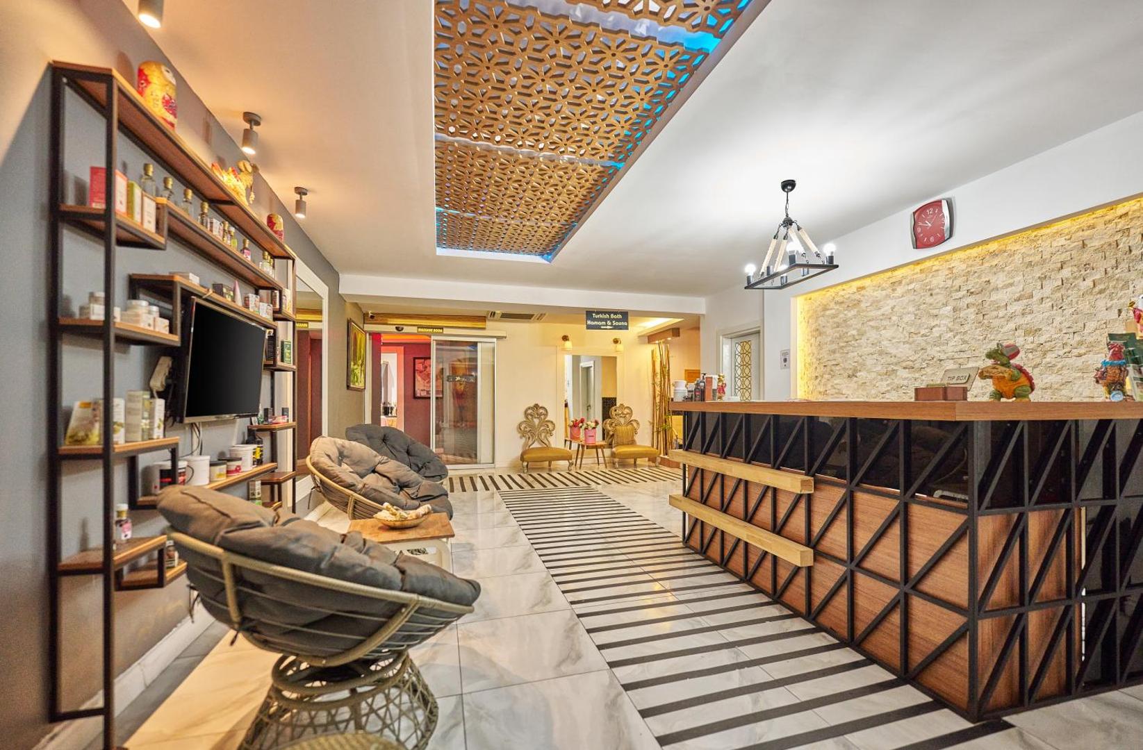 Orange County Kemer viesnīcas vestibila uzņemšanas zona ar modernu koka leti, atpūtas krēsliem un dekoratīviem griestu elementiem Turcijā