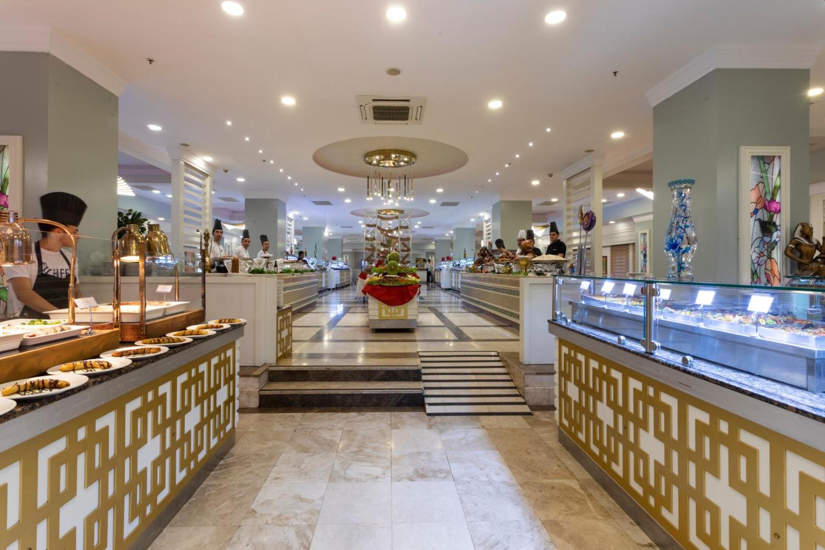 Orange County Kemer galvenā restorāna bufetes zona ar plašu ēdienu izvēli, marmora grīdu un modernu apgaismojumu Kemeras viesnīcā