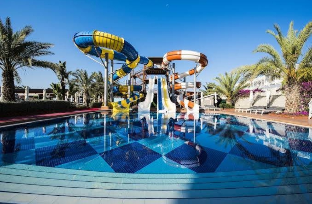 Quattro Beach Spa & Resort akvaparks ar krāsainiem ūdens slidkalniņiem un zilu baseinu palmu ieskāvumā Turcijas piekrastē