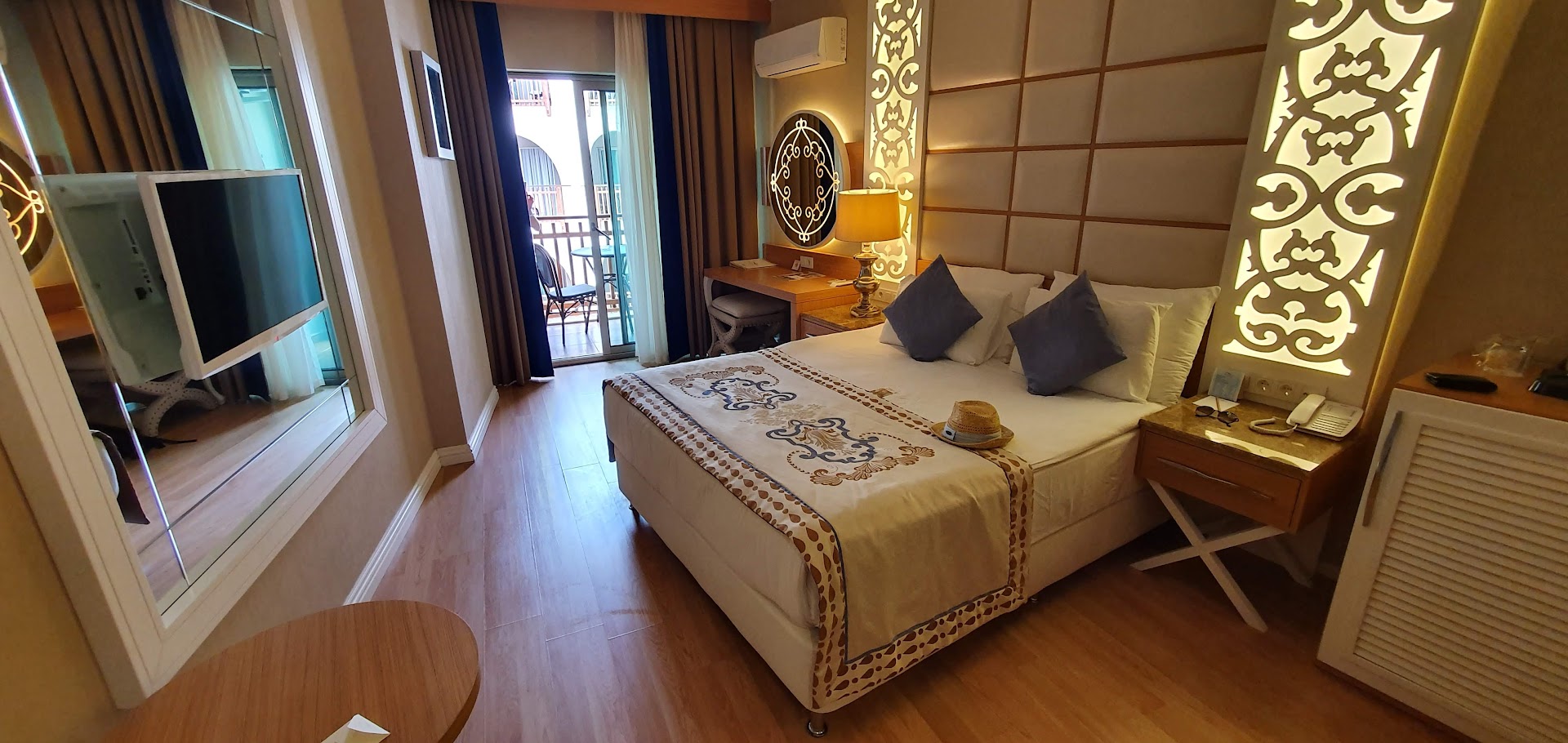 Quattro Beach Spa & Resort numura interjers ar skatu uz balkonu, televizoru un dekoratīvu apgaismojumu Alanjas piekrastē