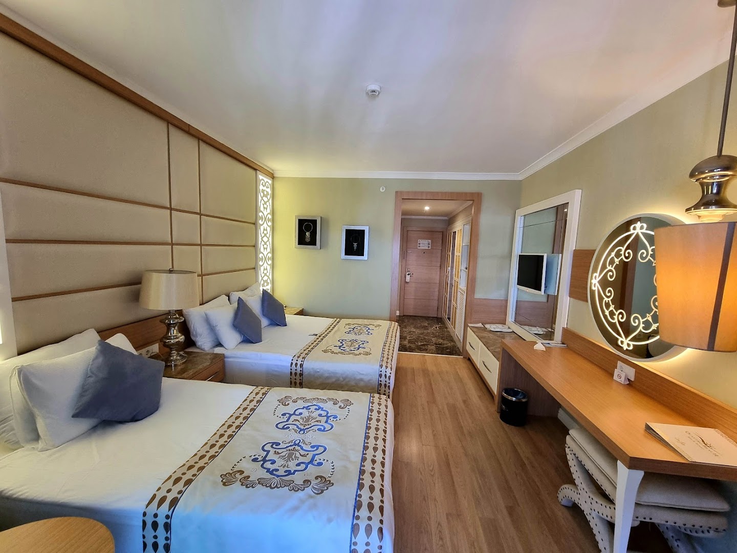 Quattro Beach Spa & Resort gaišs numurs ar divām gultām, koka grīdu, rakstainiem gultas pārklājiem un modernu apgaismojumu Alanjas reģionā