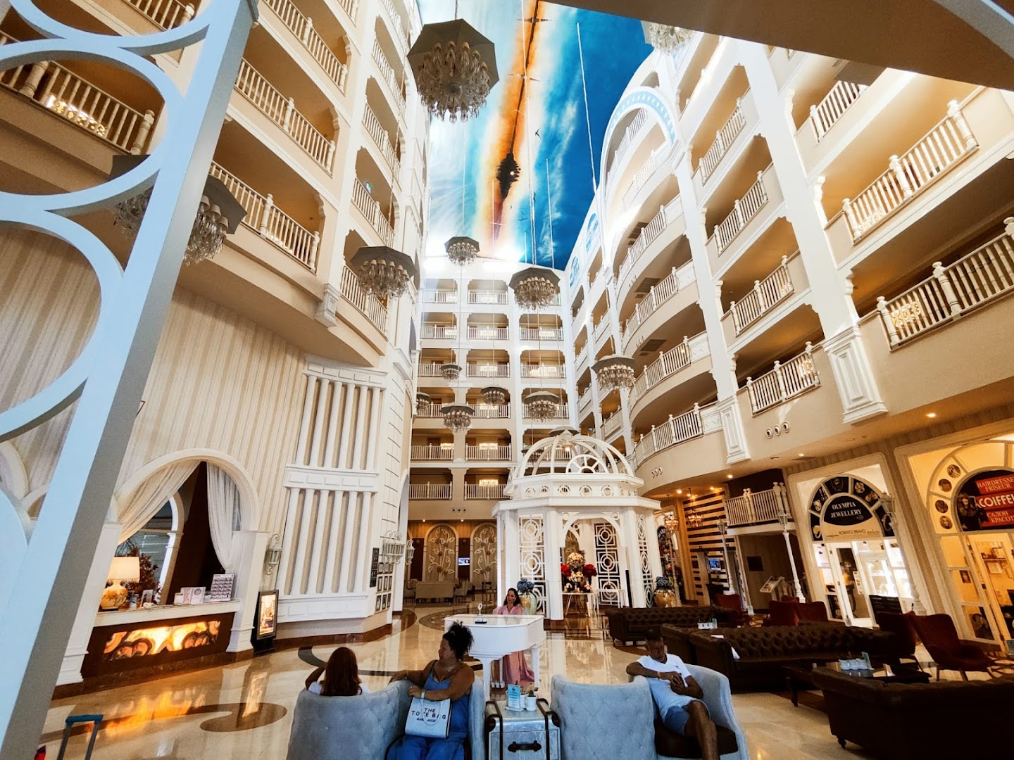 Quattro Beach Spa & Resort iespaidīgais vestibils ar augstiem griestiem, dekoratīvu kupolu, lustrām un atpūtas zonu ar mīkstajiem krēsliem.
