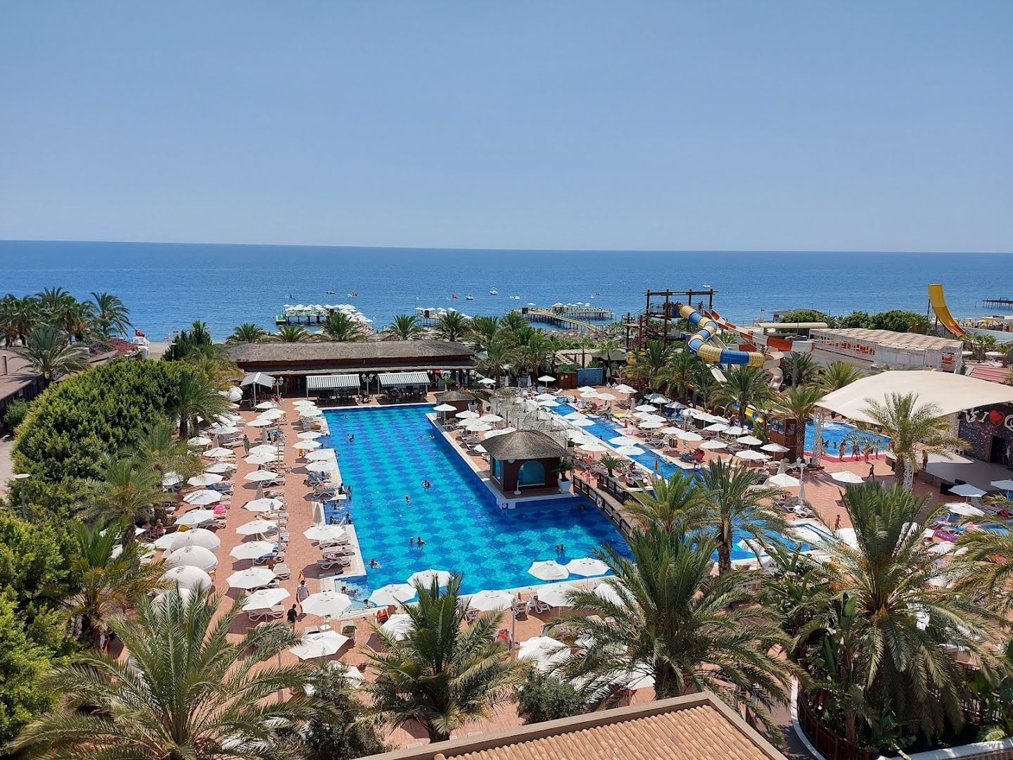 Quattro Beach Spa & Resort panorāmas skats uz plašo baseinu, saulessargiem un Vidusjūras zilgmi Alanjas piekrastē