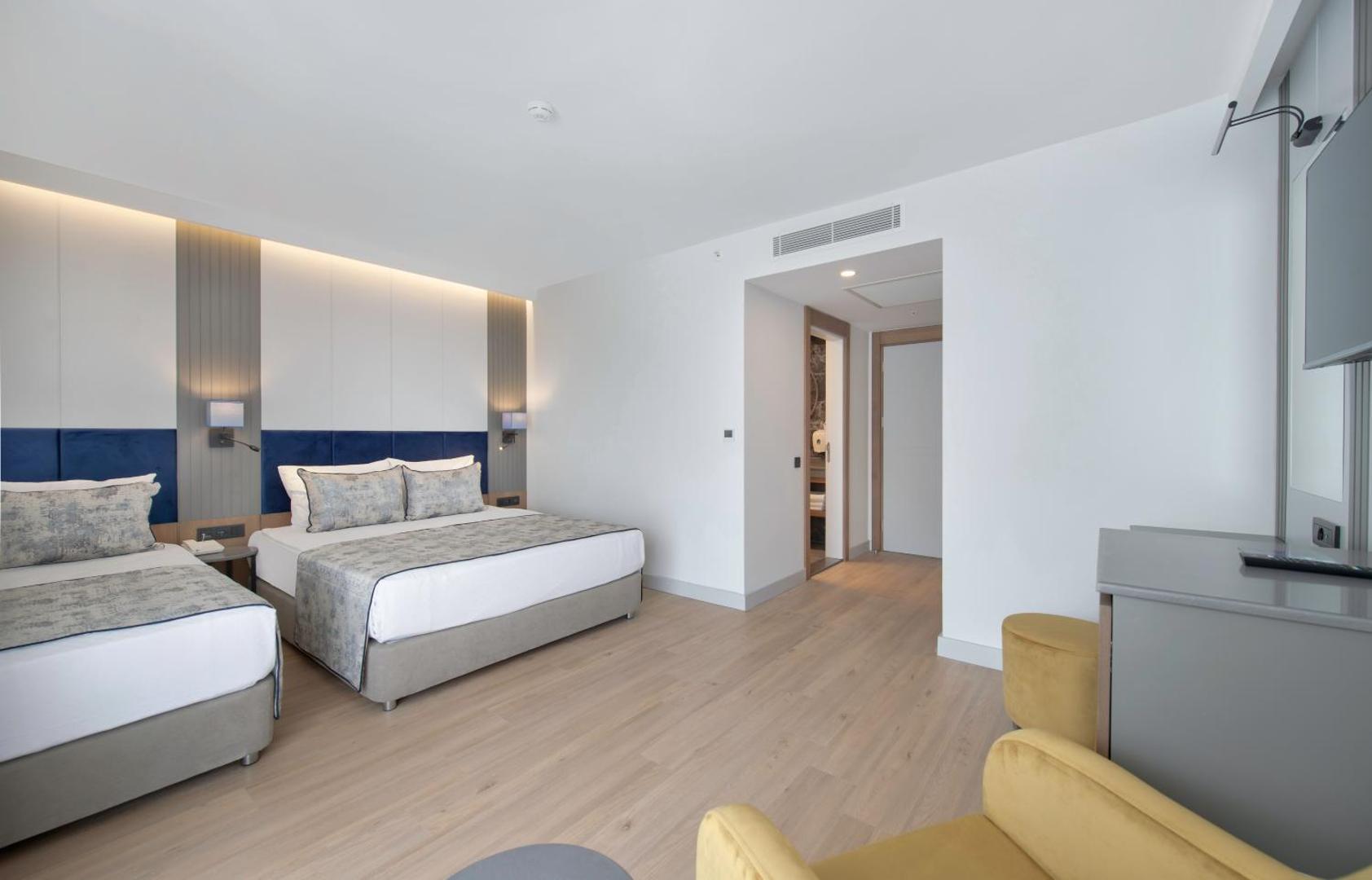 Plašs Sealife Kemer Resort ģimenes numurs ar divām gultām, ziliem galvgaļiem un dzelteniem atpūtas krēsliem