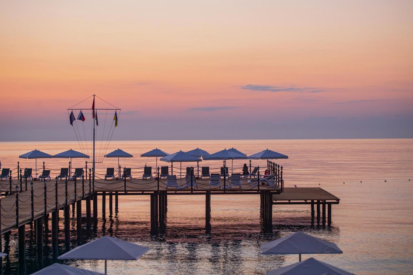 Sealife Kemer Resort Hotel koka mols virs jūras ar saulessargiem un atpūtas krēsliem romantiskā saulrieta gaismā