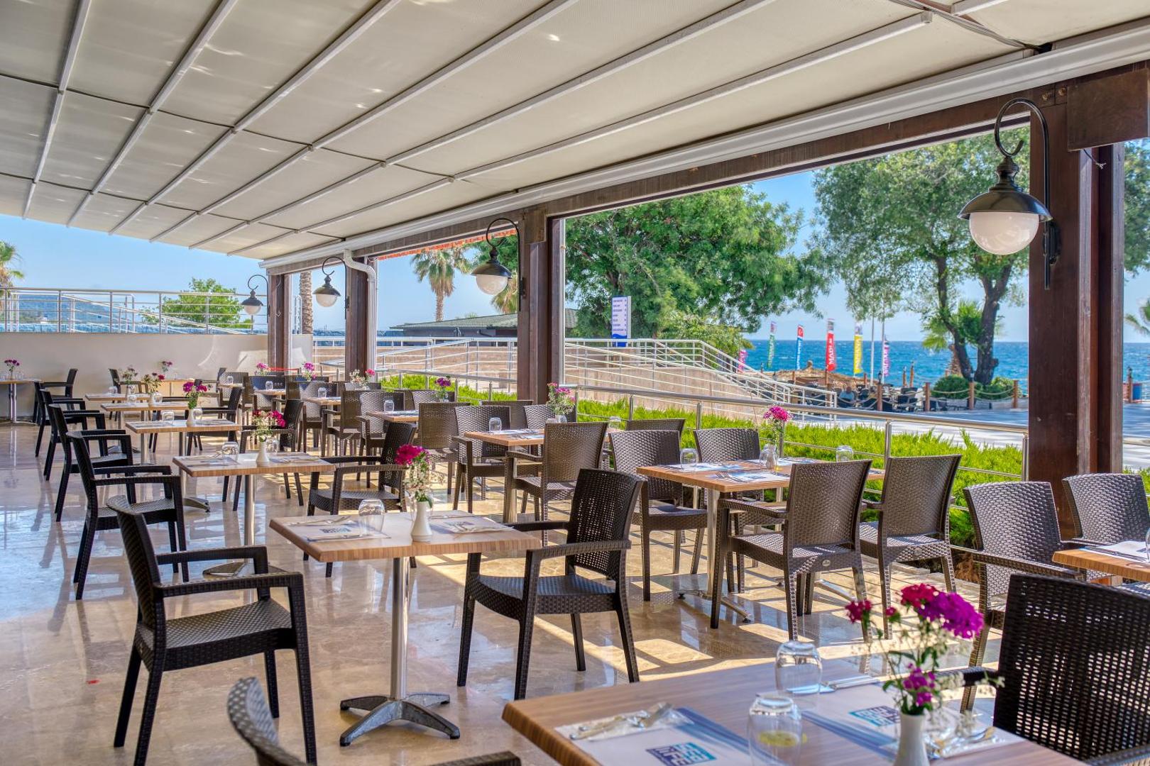 Sealife Kemer Resort Hotel āra terases restorāns ar skatu uz Vidusjūru, galdiem un pītiem krēsliem Antalijas reģionā