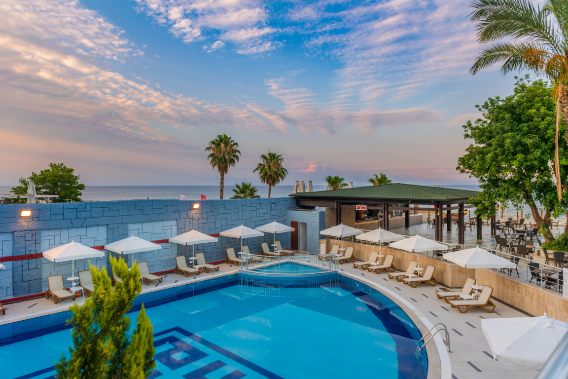 Sealife Kemer Resort Hotel āra baseins saulrietā ar skatu uz Vidusjūru, atpūtas krēsliem un saulessargiem Kemeras piekrastē