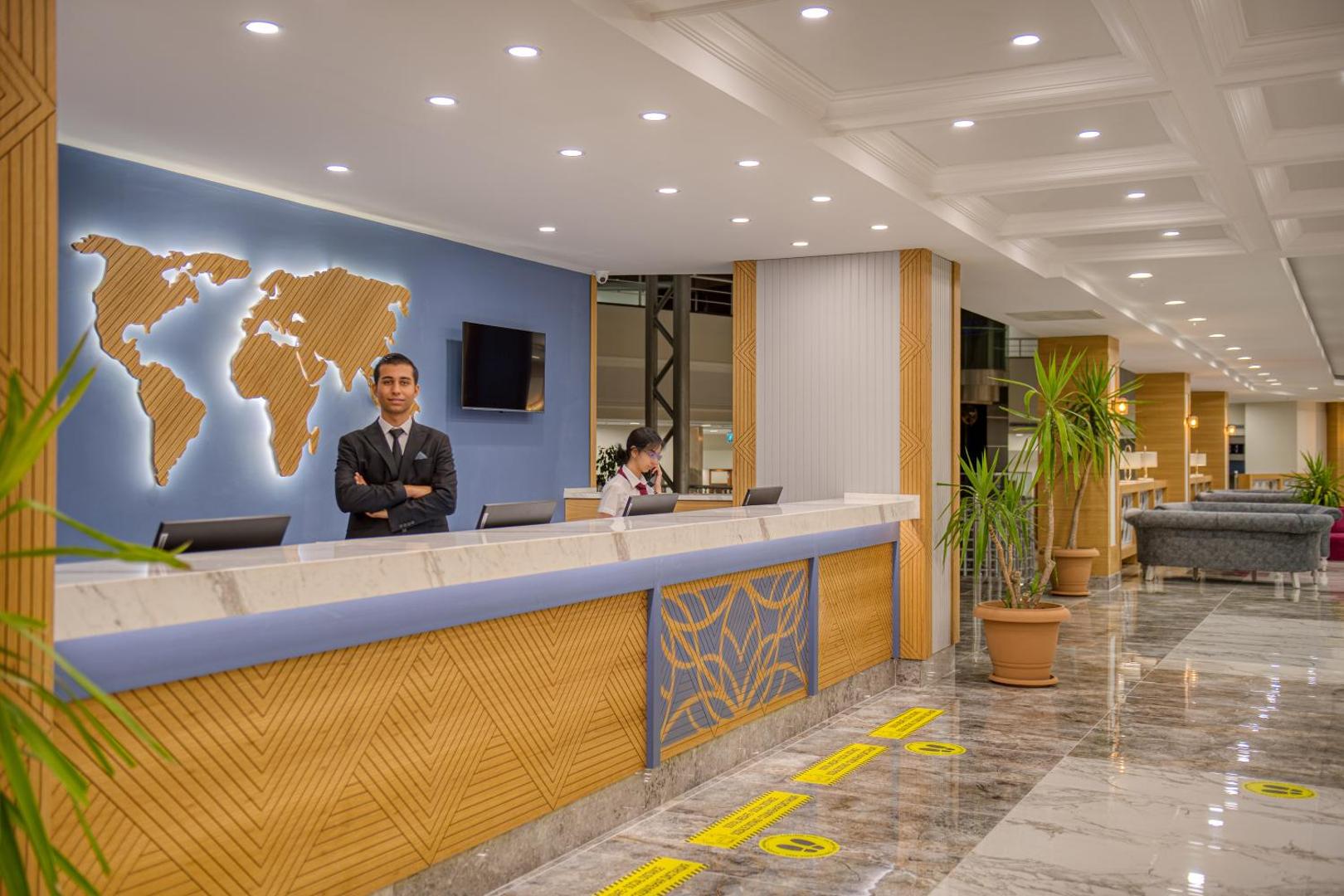 Sealife Kemer Resort Hotel modernā recepcijas zona ar marmora apdari, pasaules kartes dekoru pie sienas un viesmīlīgu personālu