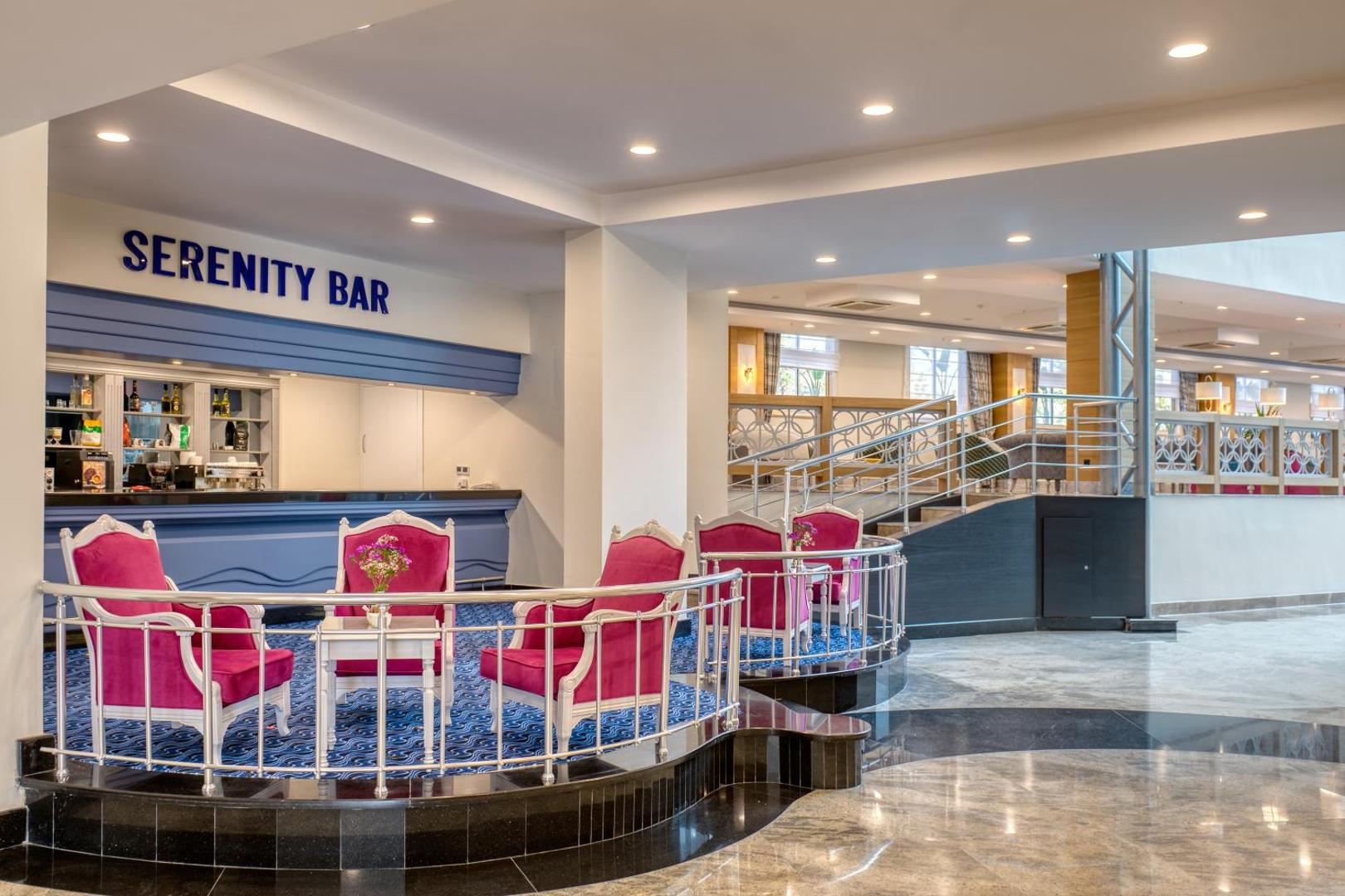 Sealife Kemer Resort Hotel vestibila bārs Serenity Bar ar rozā atpūtas krēsliem un zilu paklāju Kemerā, Turcijā