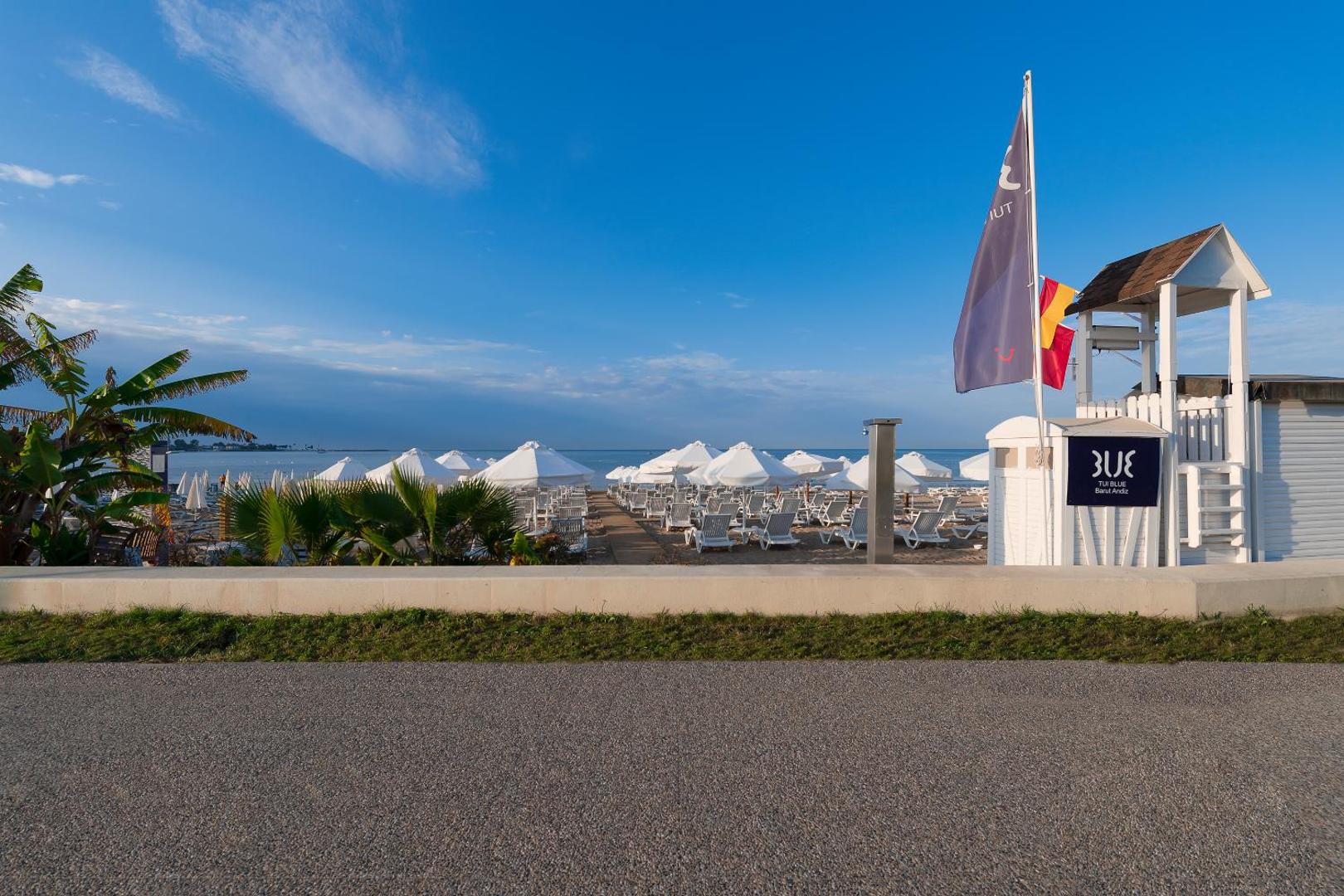 TUI BLUE Barut Andiz privātā smilšu pludmale ar baltiem saulessargiem, sauļošanās krēsliem un glābēju posteni Sidē