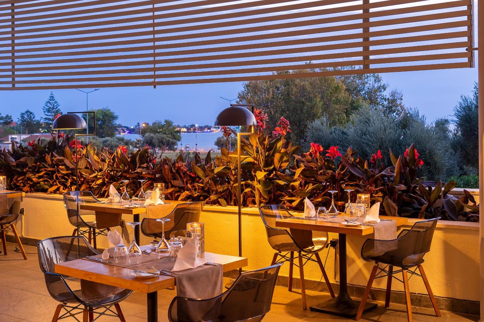 TUI BLUE Barut Andiz restorāna āra terase vakarā ar klātiem galdiem, dekoratīviem augiem un skatu uz jūru Sidē, Turcijā