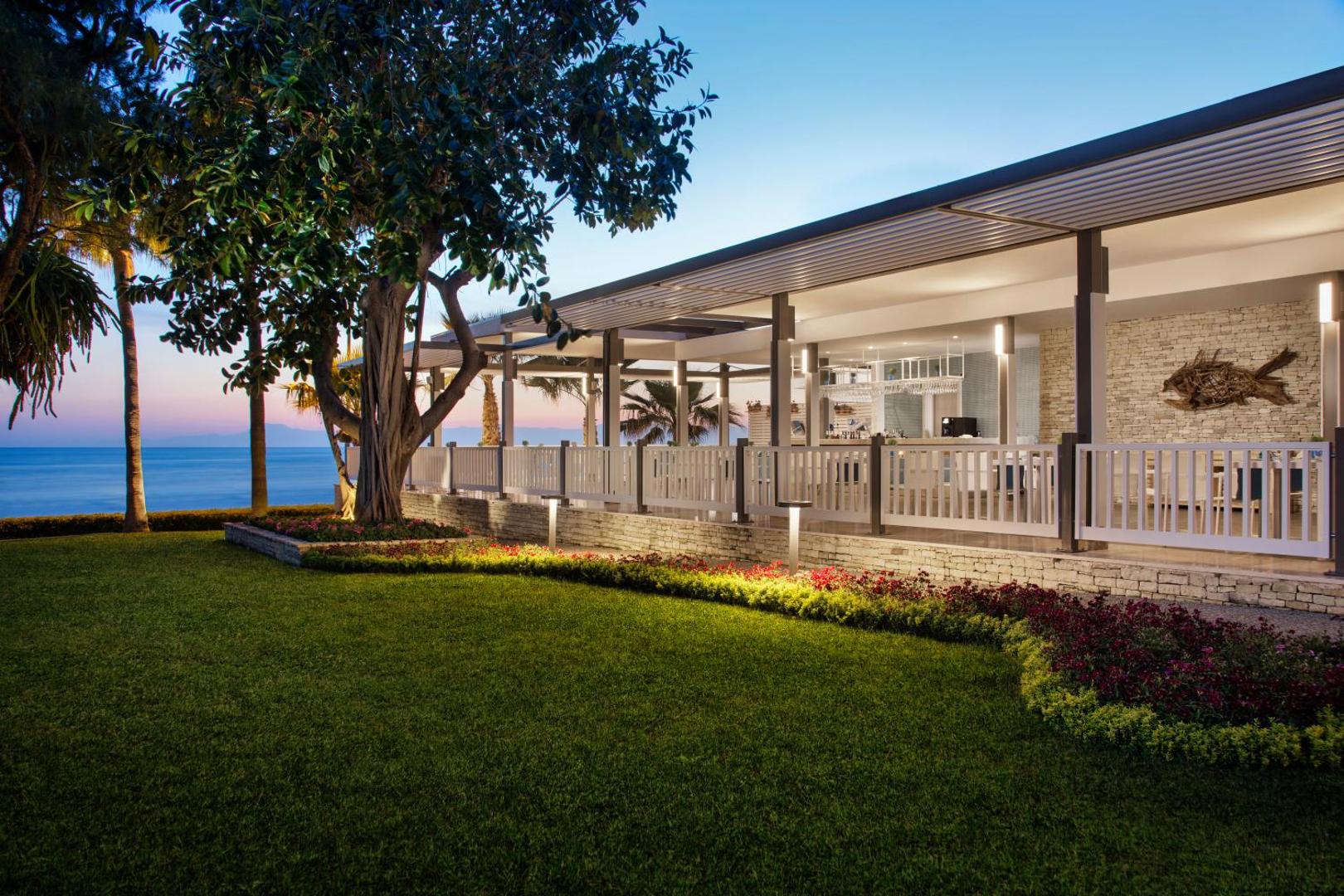 Acanthus & Cennet Barut Collection modernā restorāna terase vakarā ar apgaismotu dārzu un skatu uz jūru Sidē