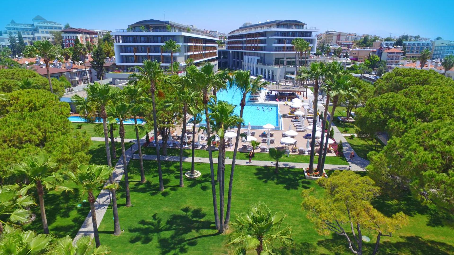 Acanthus & Cennet Barut Collection viesnīcas kopskats Sidē ar lielu āra baseinu, palmām un modernām ēkām saulainā dienā