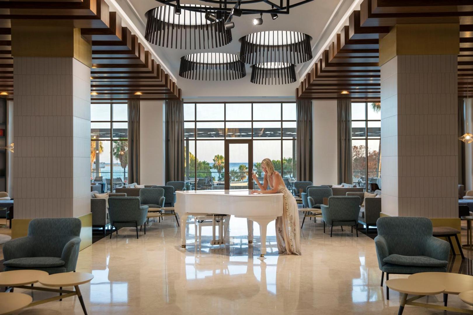 Acanthus & Cennet Barut Collection lobby bārs ar baltu flīģeli, ziliem atpūtas krēsliem un plašiem logiem uz Vidusjūras piekrasti