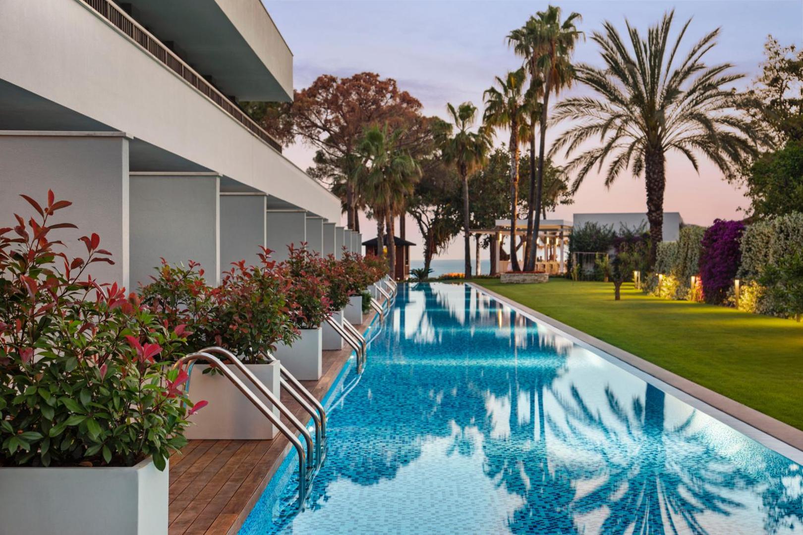 Acanthus & Cennet Barut Collection swim-up numuru privātā baseina zona ar koka terasi un zālāju vakara apgaismojumā
