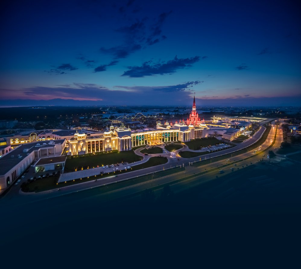 The Land of Legends Kingdom Hotel panorāmas skats naktī Belekā, Turcijā — izgaismota viesnīcas fasāde, pils torņi un apkārtējā teritorija krēslā