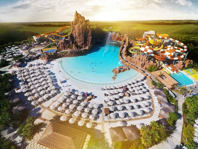 The Land of Legends Kingdom Hotel mākslīgā pludmale ar viļņu baseinu, saulessargiem un klinšu imitācijām saulrieta gaismā