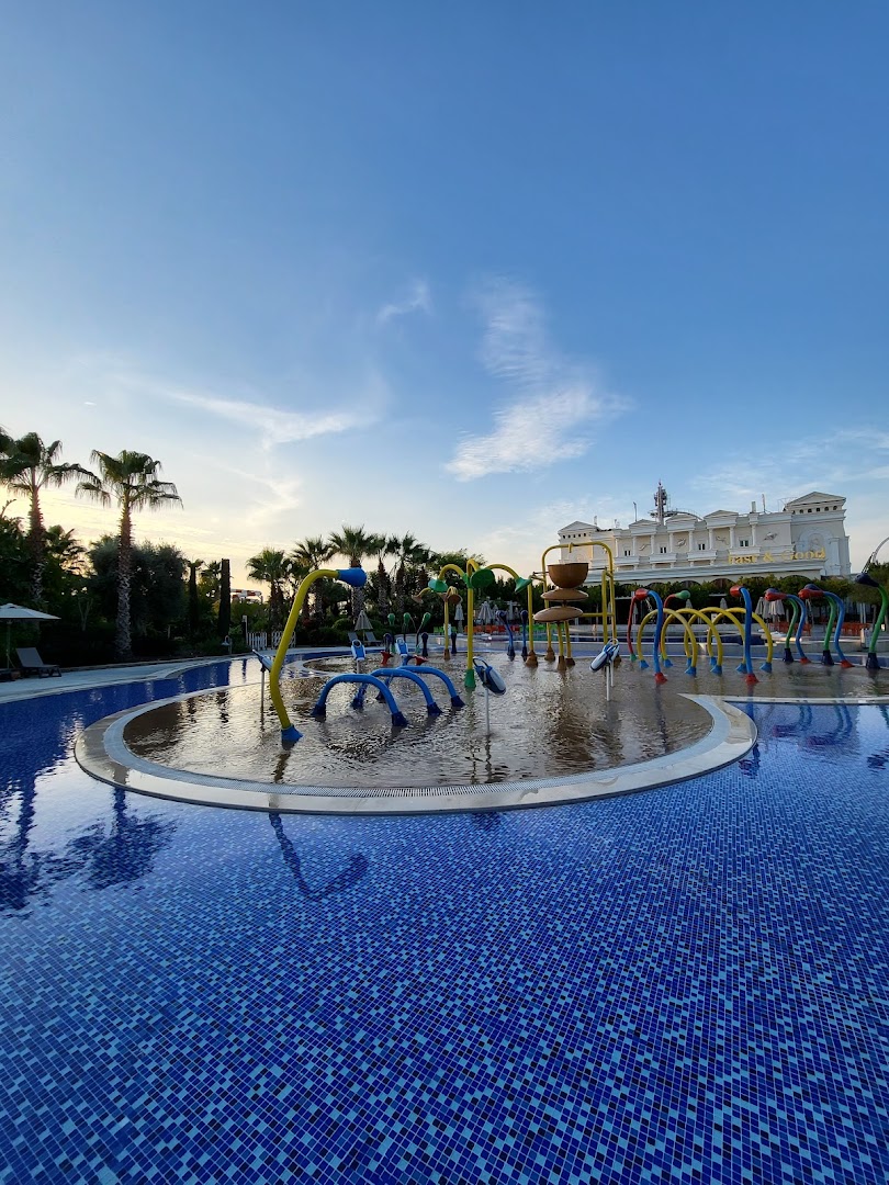 The Land of Legends Kingdom Hotel āra baseins ar bērnu ūdens strūklakām un viesnīcas ēku fonā saulrietā