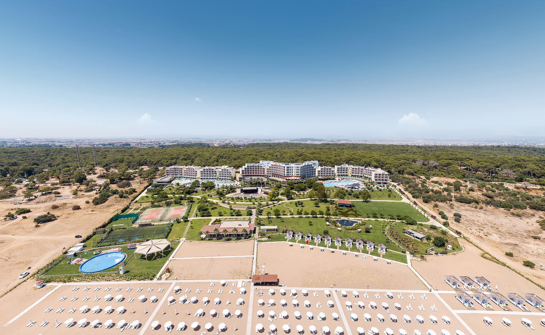 Akra Sorgun Tui Blue Sensatori teritorijas panorāma ar tenisa kortiem, bērnu baseinu un plašiem zālieniem pie jūras