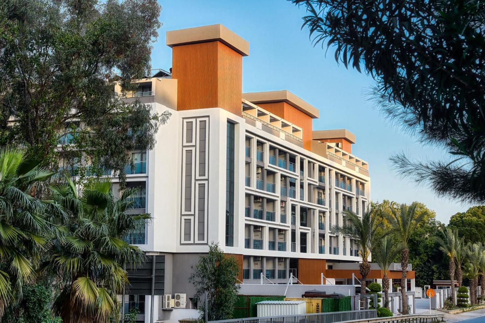 Annabella Diamond Hotel korpusa fasāde ar balkoniem, ko ieskauj zaļojoši koki un palmas Alānijas piekrastē