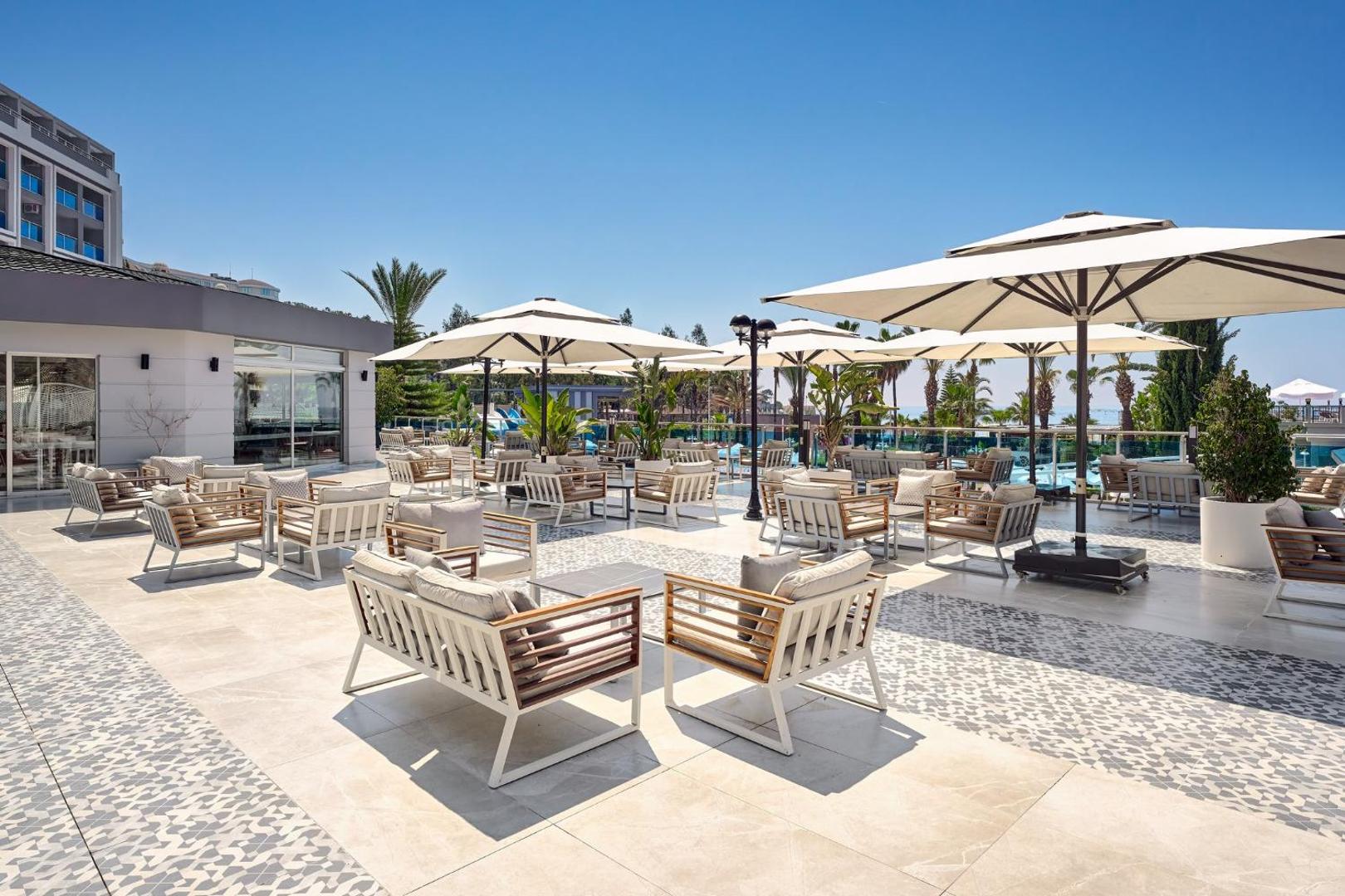 Annabella Diamond Hotel āra terase ar modernām mēbelēm un saulessargiem — plaša atpūtas zona pie baseina Alanjas piekrastē