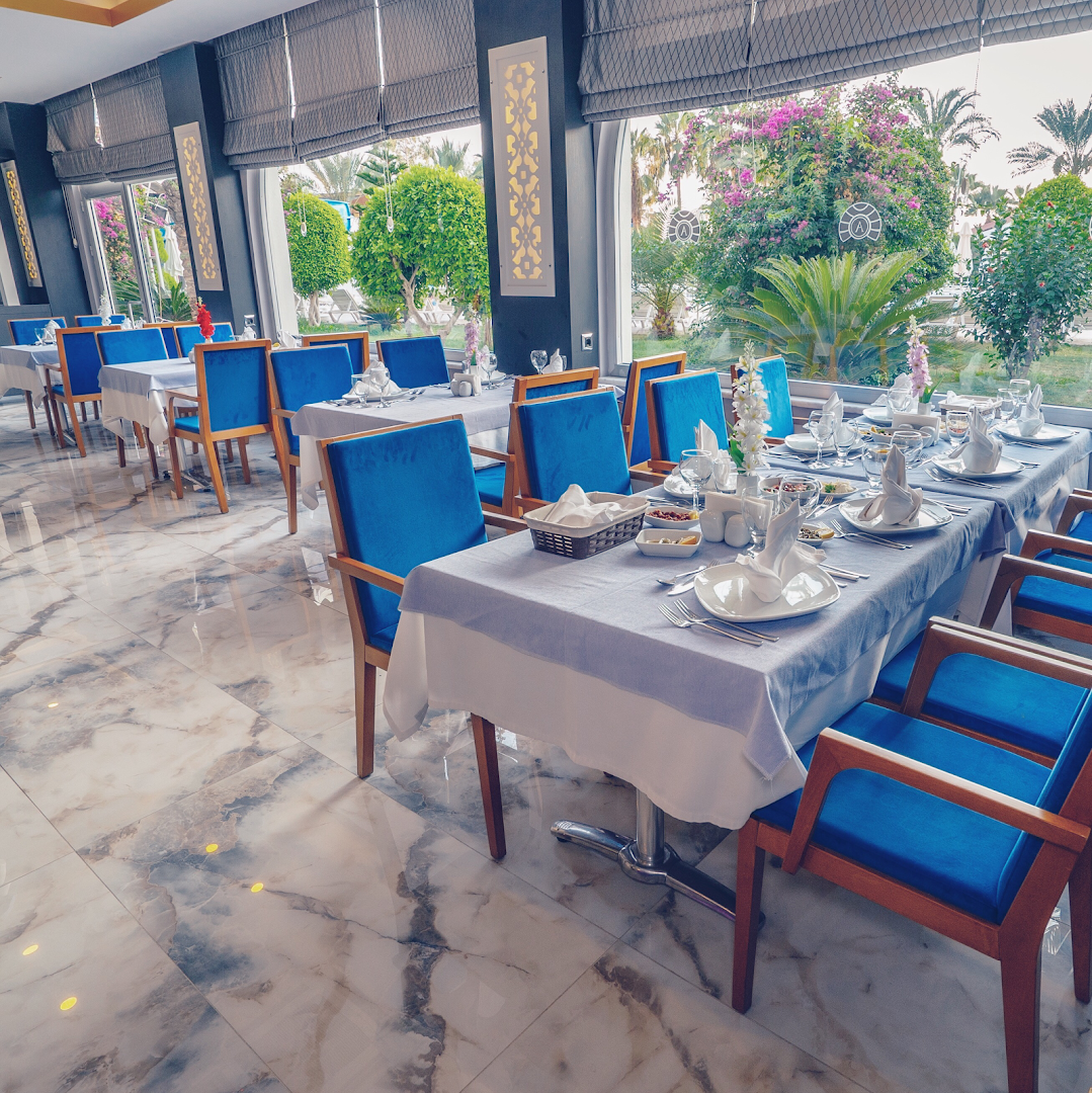 Annabella Diamond Hotel restorāns ar ziliem krēsliem un eleganti klātiem galdiem pie lieliem logiem ar skatu uz dārzu