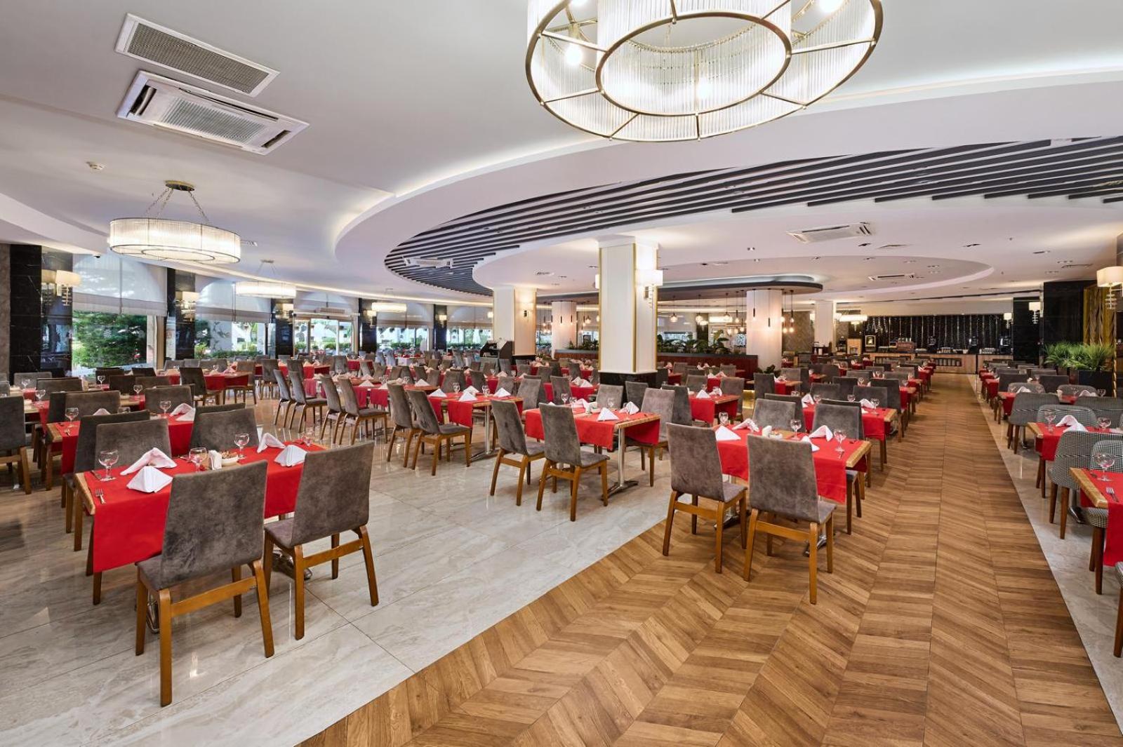 Annabella Diamond Hotel galvenais restorāns ar klātiem galdiem, sarkaniem galdautiem un modernu apgaismojumu plašā, gaišā telpā