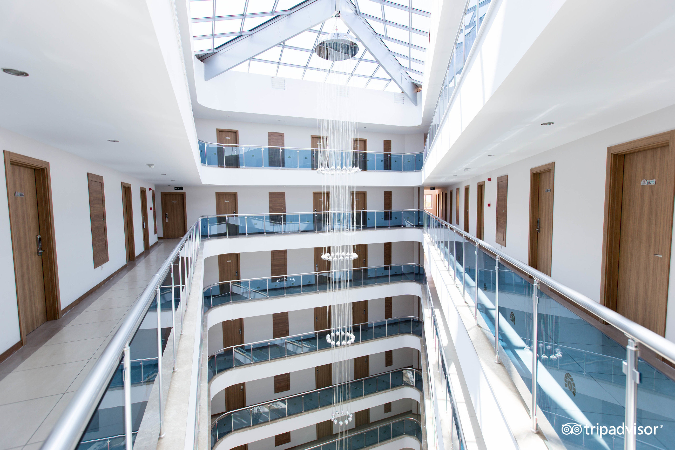 Annabella Diamond Hotel modernais ātrijs ar stikla jumtu un daudzstāvu gaiteņiem — gaišs interjers ar iespaidīgu kristāla lustru centrā