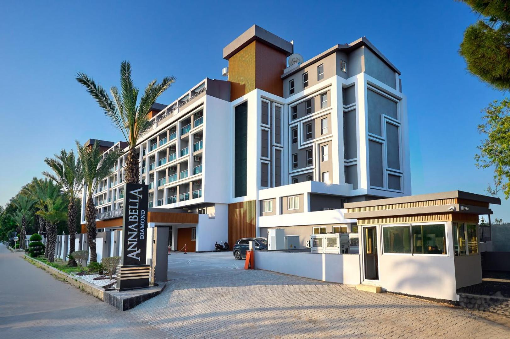 Annabella Diamond Hotel galvenā ieeja un modernā fasāde ar palmām un viesnīcas nosaukuma zīmi saulainā dienā