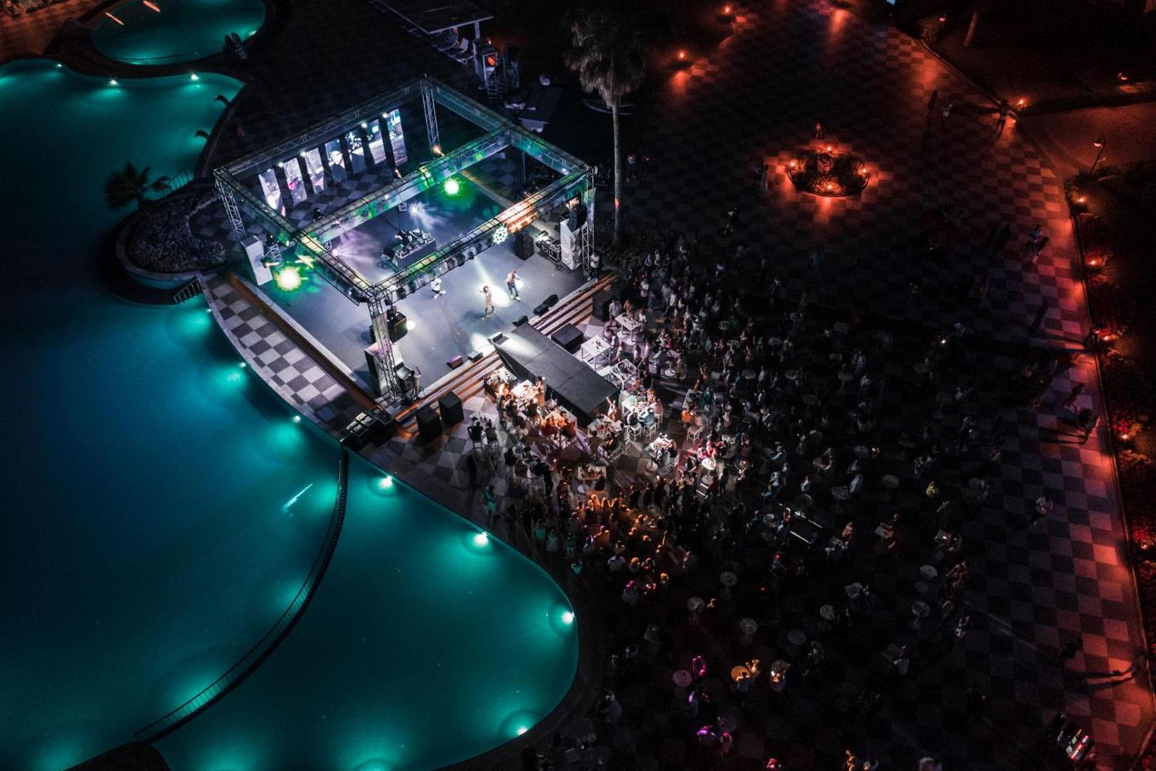 Club Marco Polo vakara izklaides pasākums pie baseina Kemeras reģionā — skats no augšas uz izgaismotu skatuvi un viesu pūli