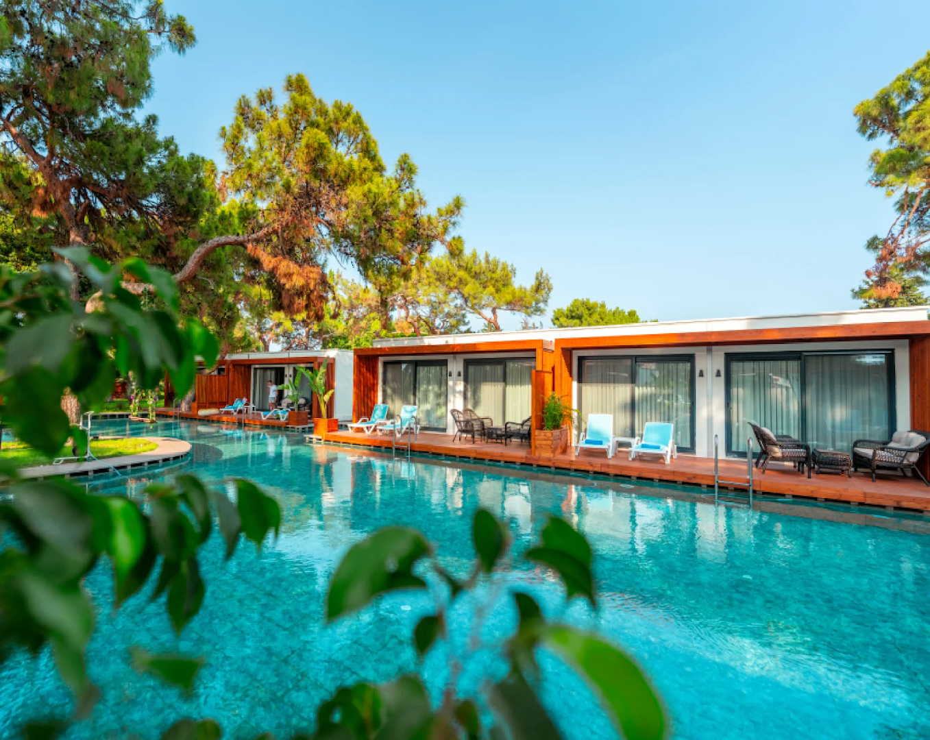 Club Marco Polo bungalo rinda pie baseina ar koka klājiem un atpūtas krēsliem priežu dārzā Kemeras kūrortā