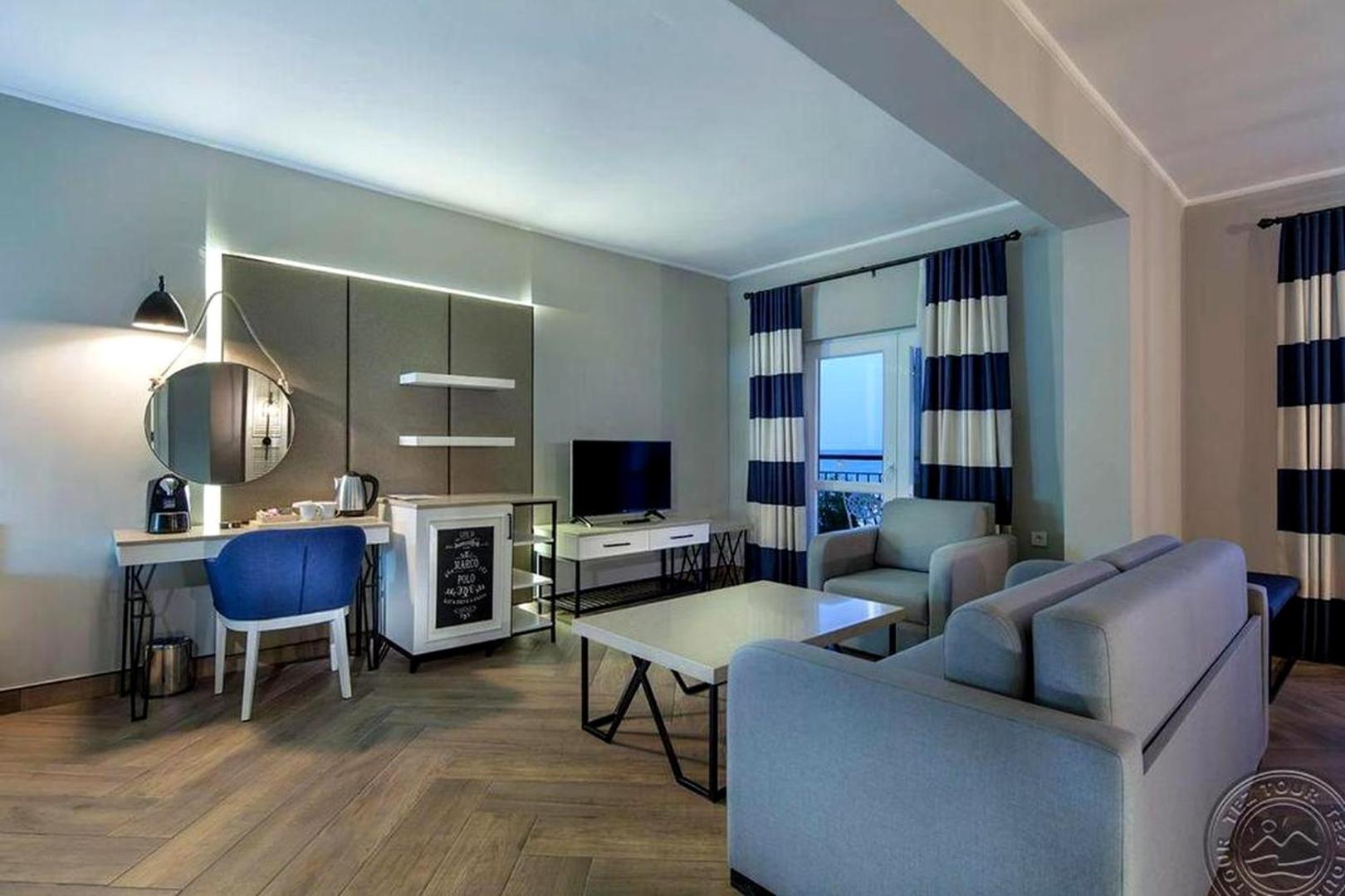 Club Marco Polo plaša viesistabas zona ar pelēku dīvānu, atpūtas krēsliem un TV zonu Kemeras viesnīcā