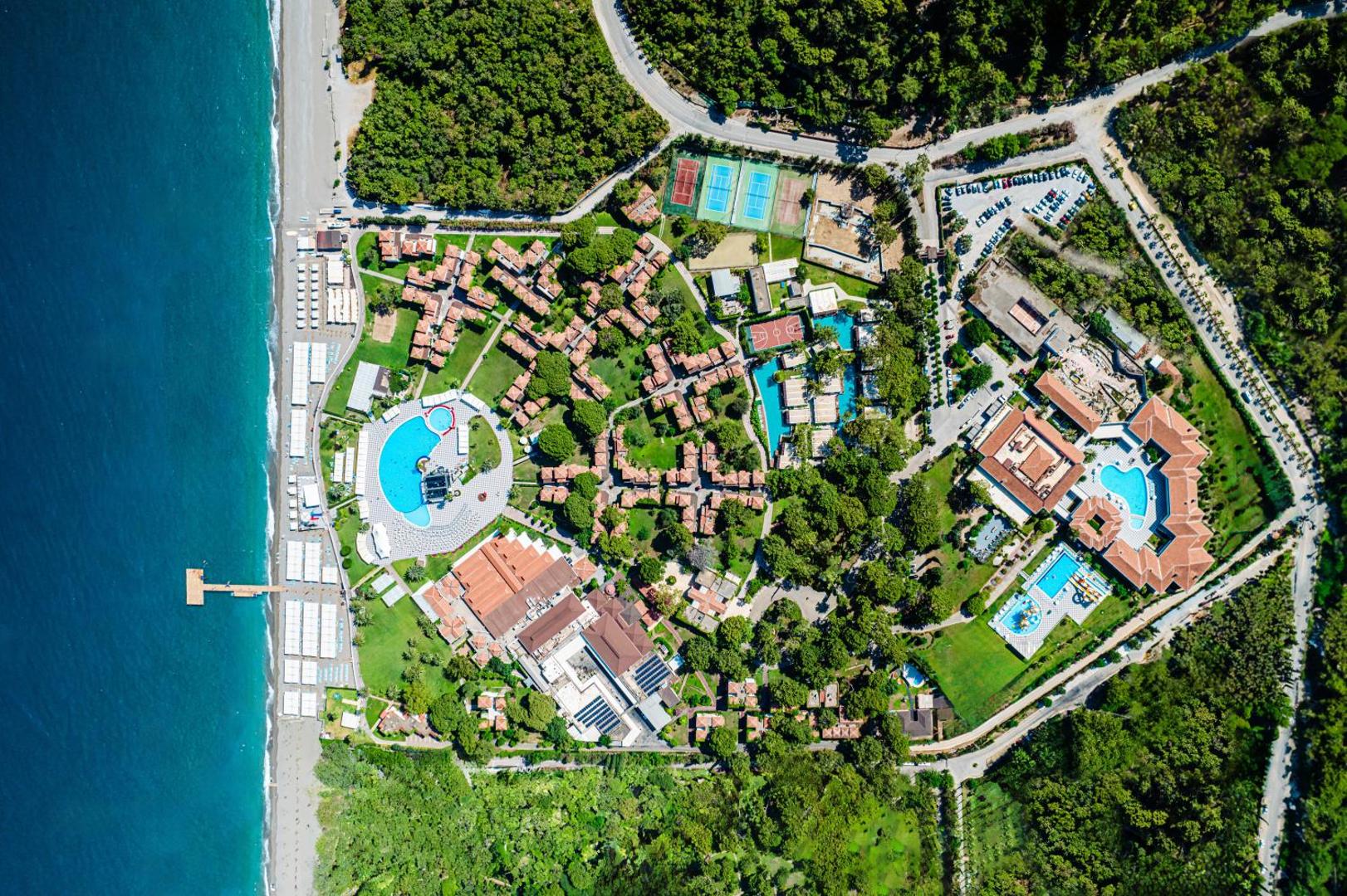 Club Marco Polo viesnīcas plānojums no augšas — redzami tenisa korti, vairāki baseini, dārzi un ēku izvietojums pie jūras