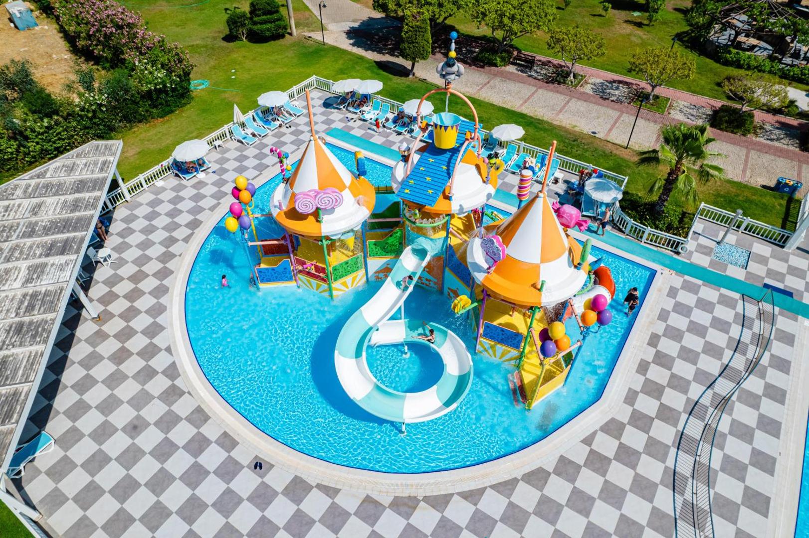 Club Marco Polo bērnu akvaparks no putna lidojuma — krāsaini slidkalniņi, sekls baseins un sauļošanās zona ar lietussargiem