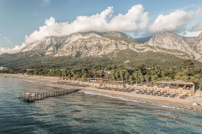 Balmy Beach Resort Kemer panorāmas skats no jūras puses uz privāto pludmali, piestātni un iespaidīgajiem Taurus kalniem fonā