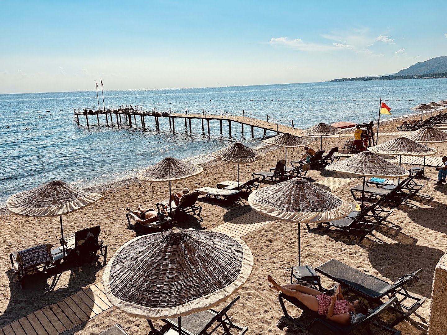 Skats no augšas uz Balmy Beach Resort Kemer pludmali ar koka piestātni un atpūtniekiem sauļošanās krēslos