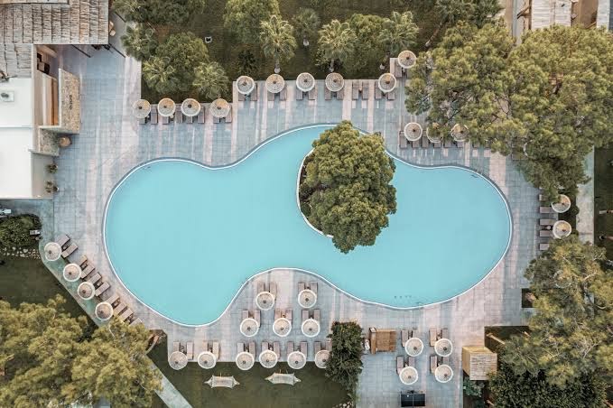 Balmy Beach Resort Kemer galvenais baseins no putna lidojuma — unikālas formas baseins ar atpūtas krēsliem un zaļo zonu