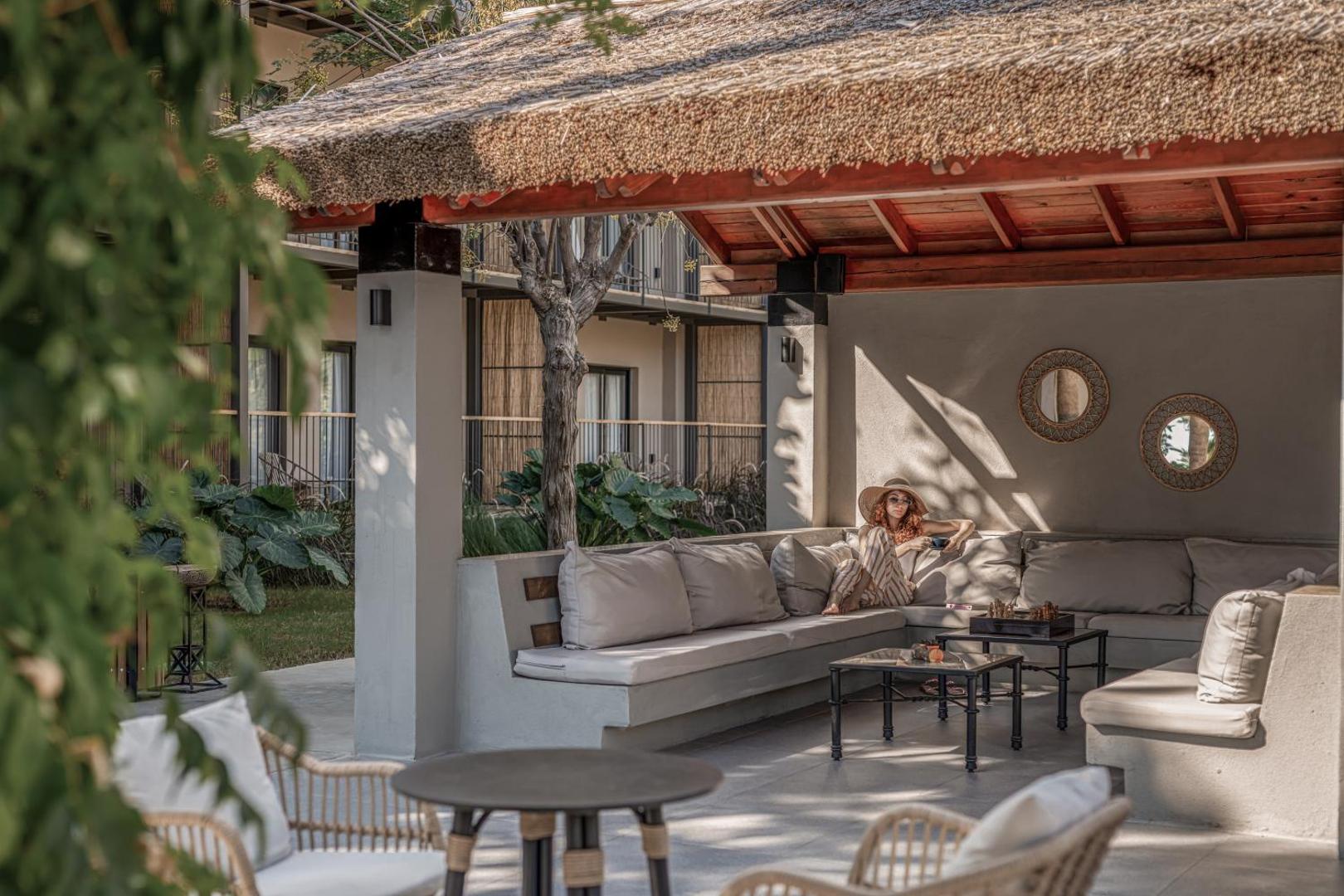 Balmy Beach Resort Kemer āra atpūtas zona ar salmu jumtu, mīkstiem dīvāniem un sievieti atpūšoties dārza ielokā